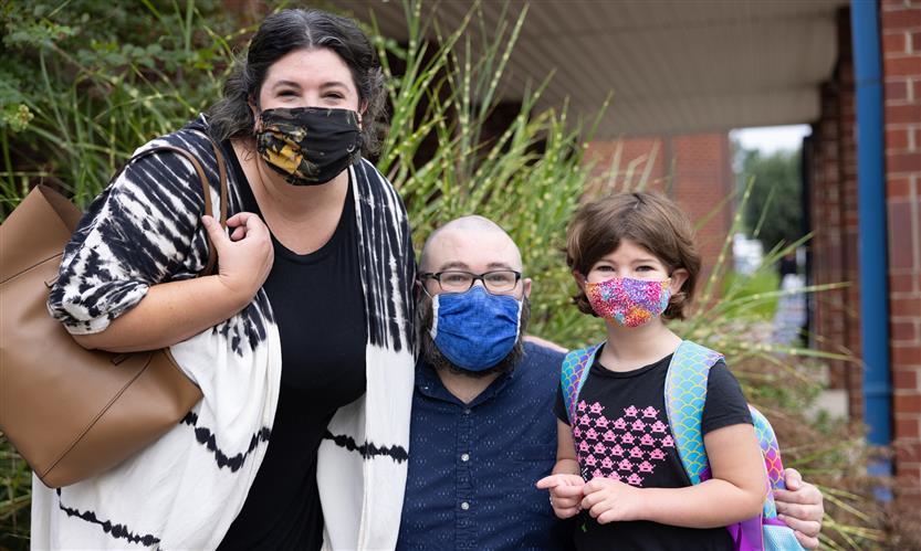 A family smiles as they arrive on the first full day of kindergarten